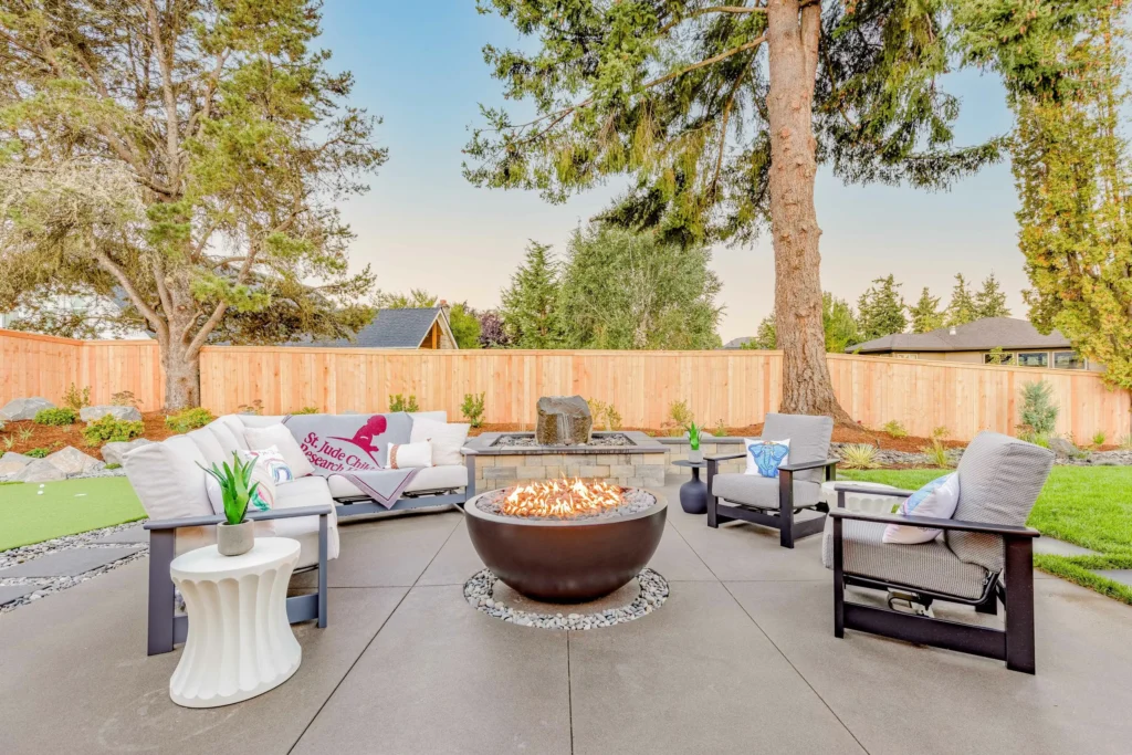 Landscaped backyard patio with round fire pit, outdoor seating area, and wooden privacy fence at 11506 NW 41st Ct - Marnella Homes custom home