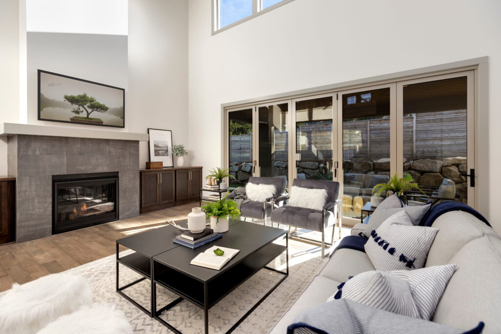 Modern living room with a fireplace, grey sofa, black coffee table, and glass sliding doors leading to a backyard.