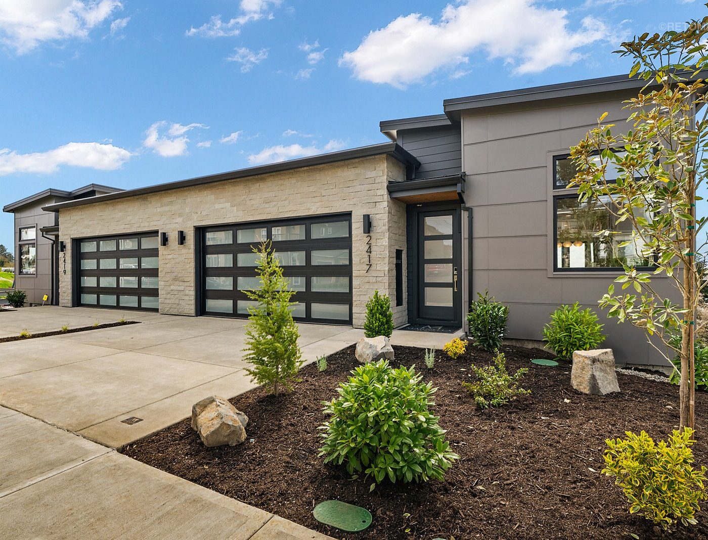 Modern single-story home with a grey and stone exterior, two-car garage, and manicured landscaping.