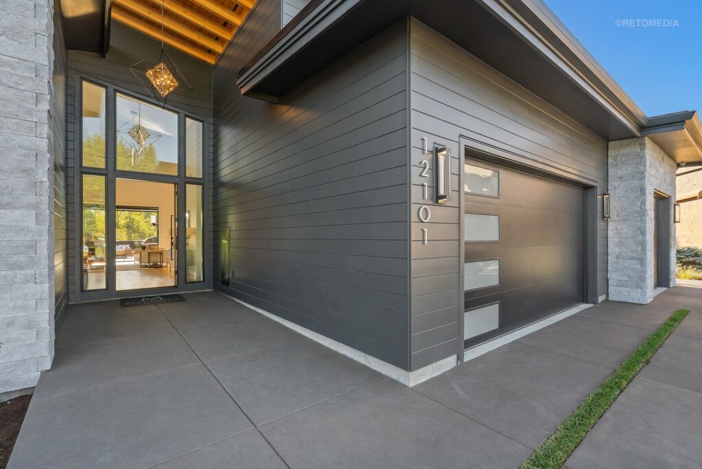 Modern dark gray home exterior with a glass front door, a garage, and vertical address numbers 12101.