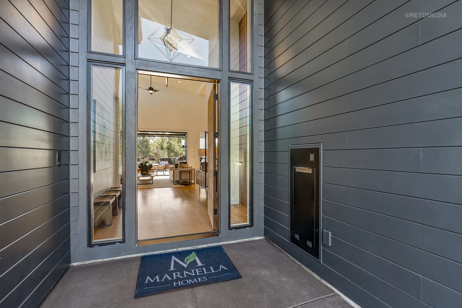 Modern entryway with grey siding, large glass doors, and a Marnella Homes welcome mat.