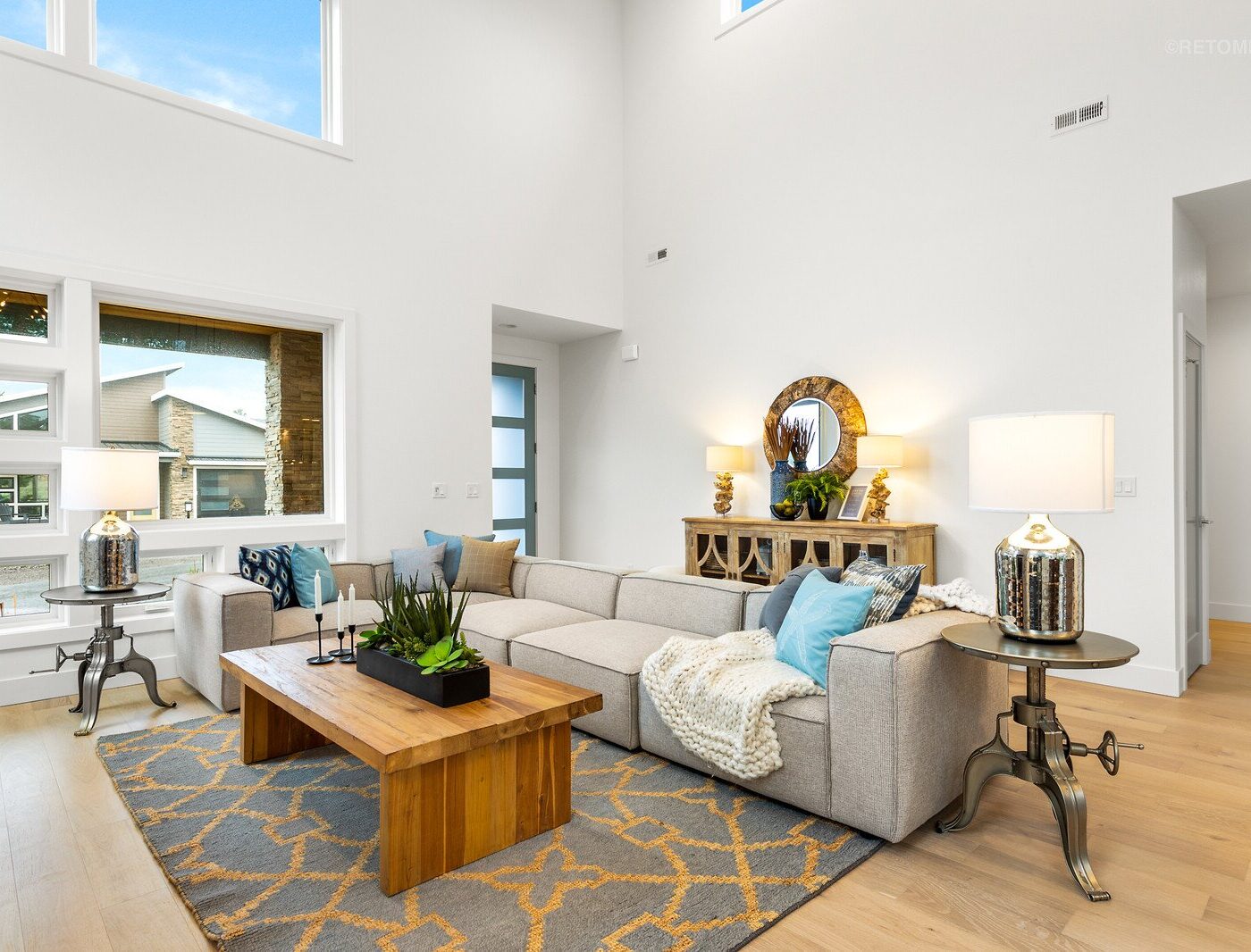 Bright modern living room with a large gray sectional sofa, wooden coffee table, and high ceilings.
