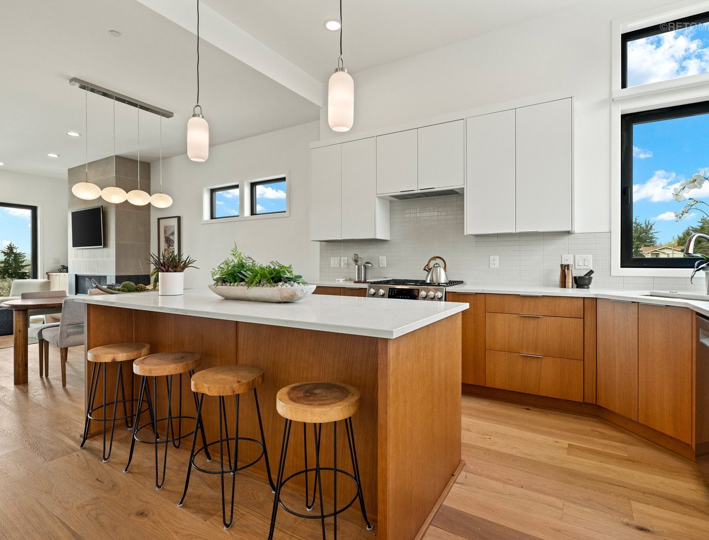 Modern kitchen with white upper cabinets, wood lower cabinets, a large white island, and four wooden stools.