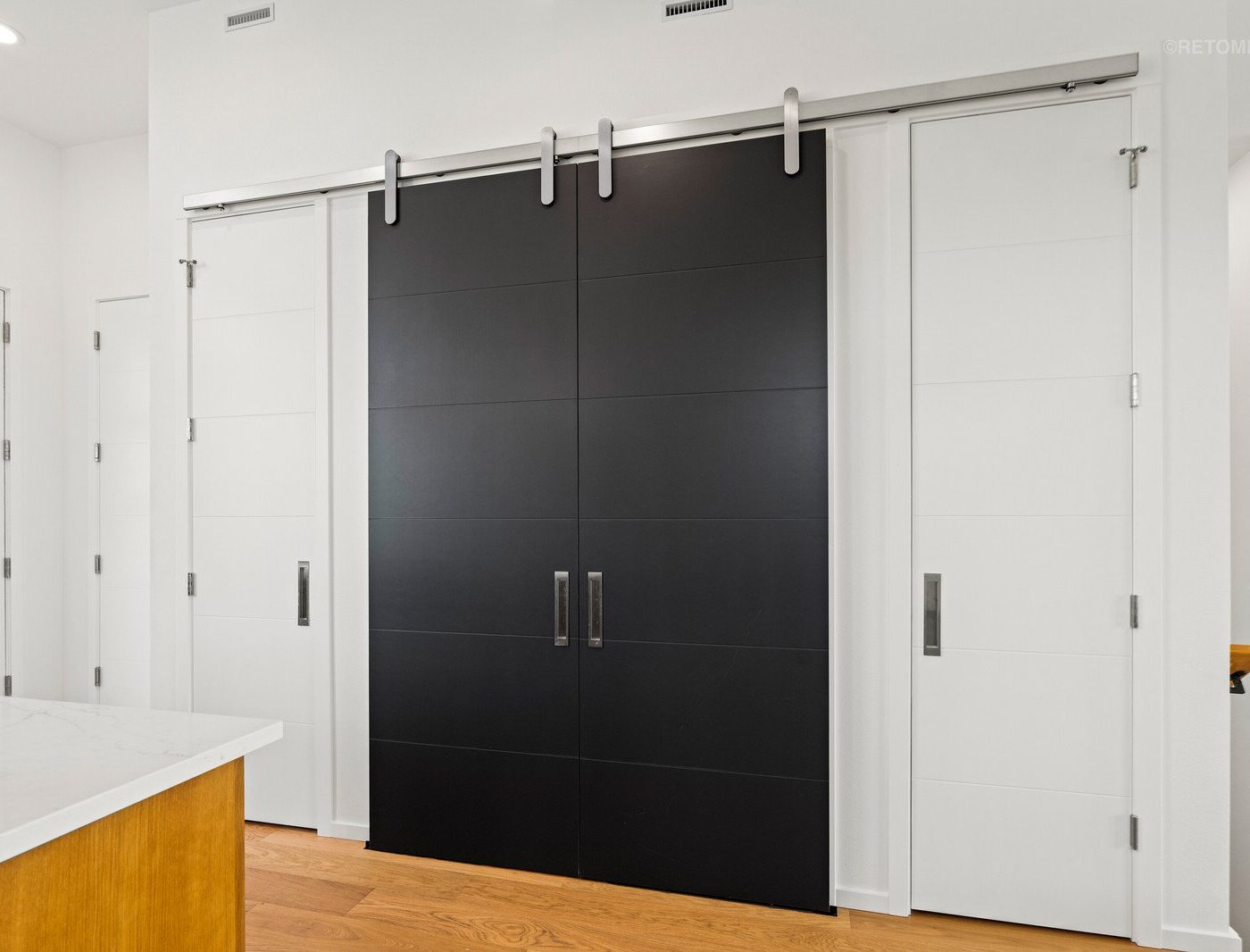 Modern interior with a sliding black double door flanked by two white doors and light wood flooring.