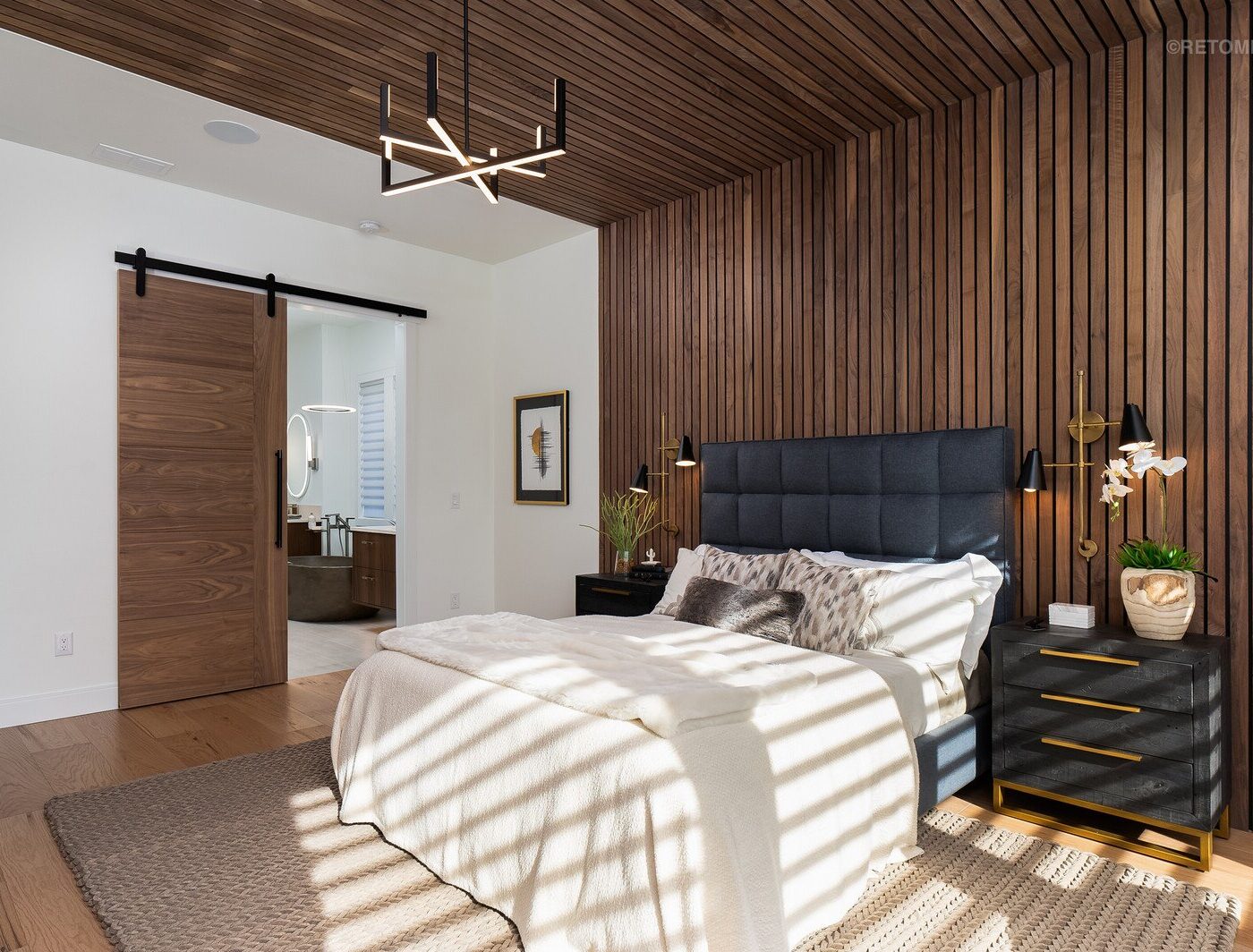 Modern bedroom with dark wood slat walls and ceiling, a grey upholstered bed, and a sliding barn door.