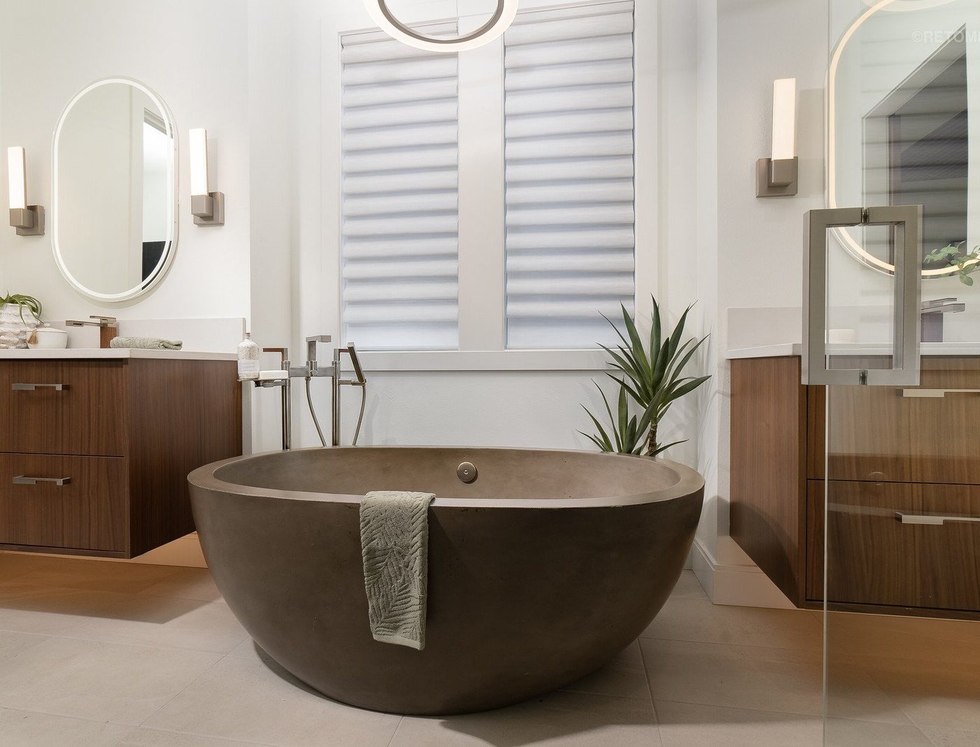 Modern bathroom with a freestanding concrete soaking tub, double wooden vanities, and frosted windows.
