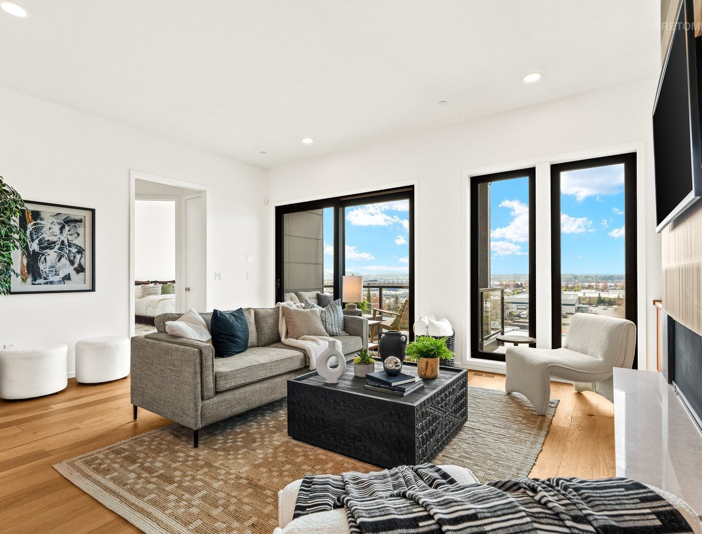 Modern living room with a grey sofa, black coffee table, and large windows overlooking a city skyline.