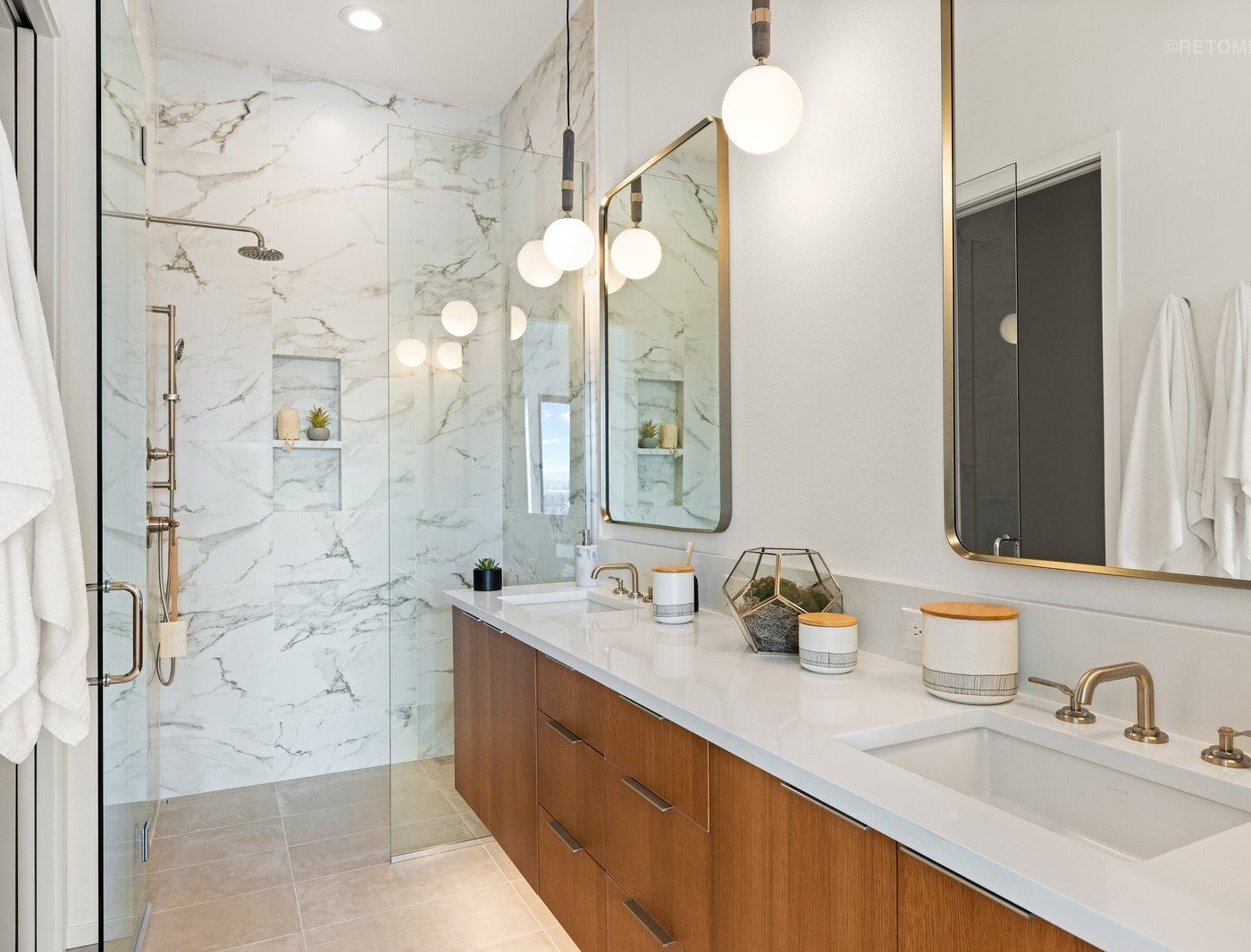 Modern bathroom with a marble walk-in shower, gold fixtures, wood vanity with white countertop, and gold-framed mirrors.