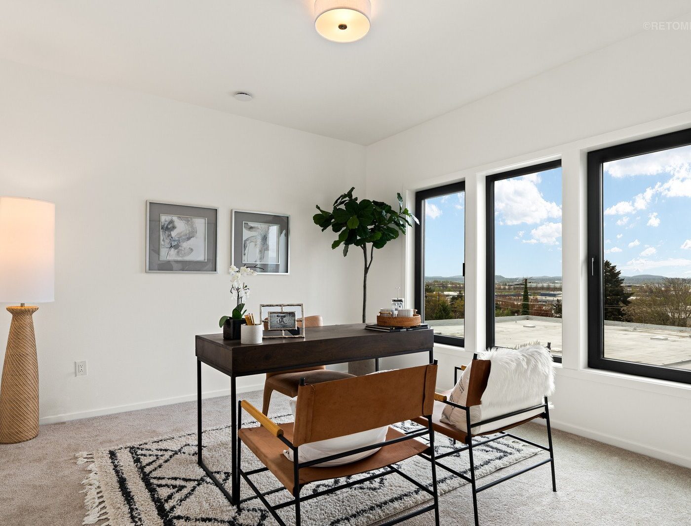 Bright home office with a dark wood desk, leather chairs, and large windows overlooking a city view.