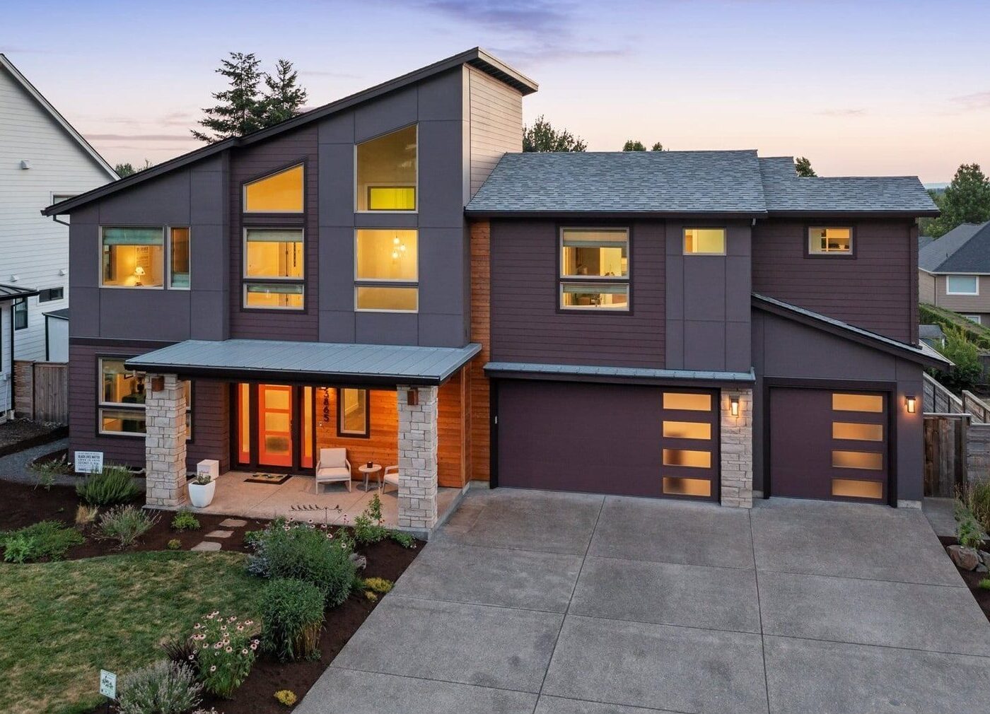 Modern two-story home with a slanted roof, purple-grey siding, and a two-car garage at dusk.