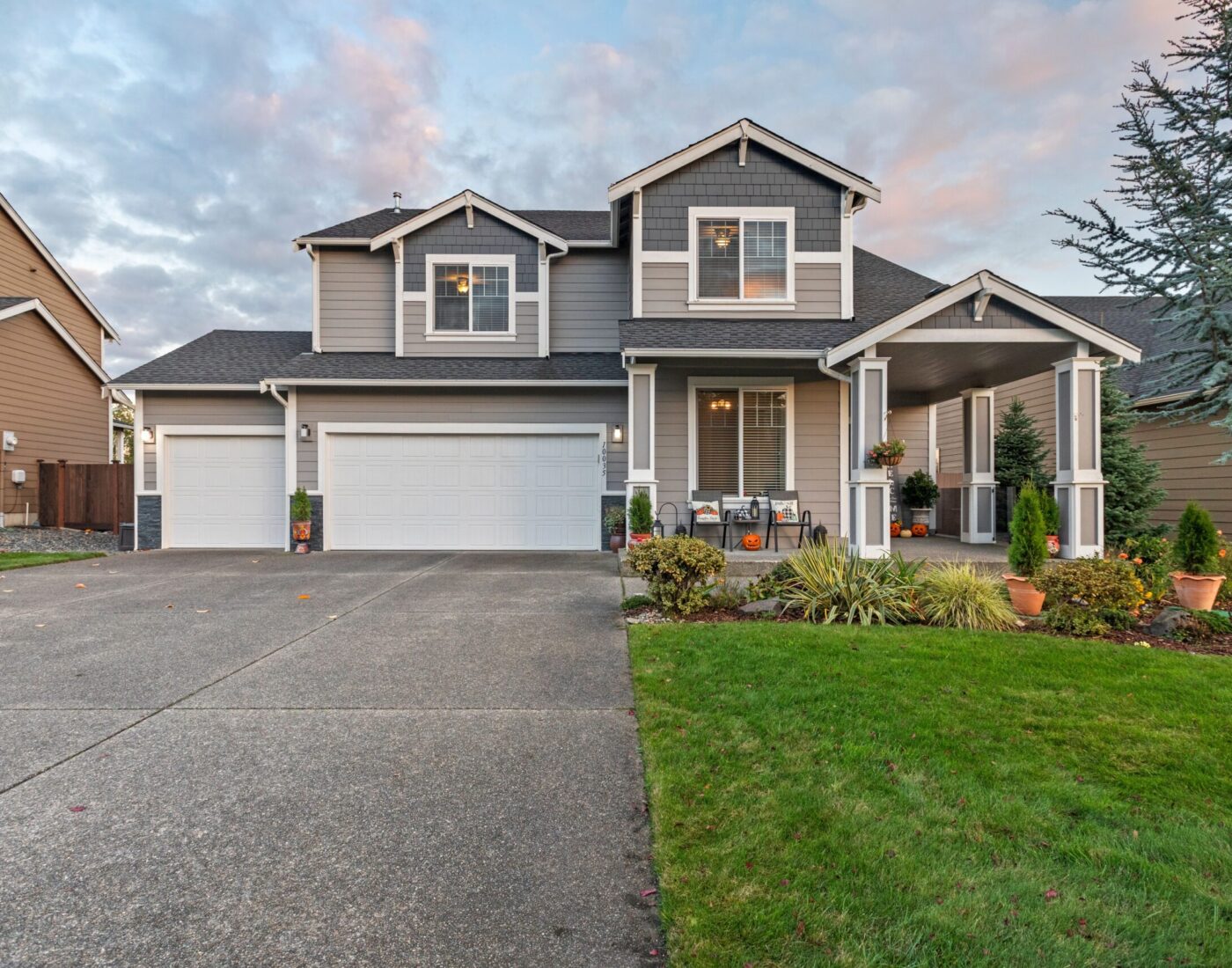 Two-story gray suburban home with a two-car garage, concrete driveway, and manicured green lawn.