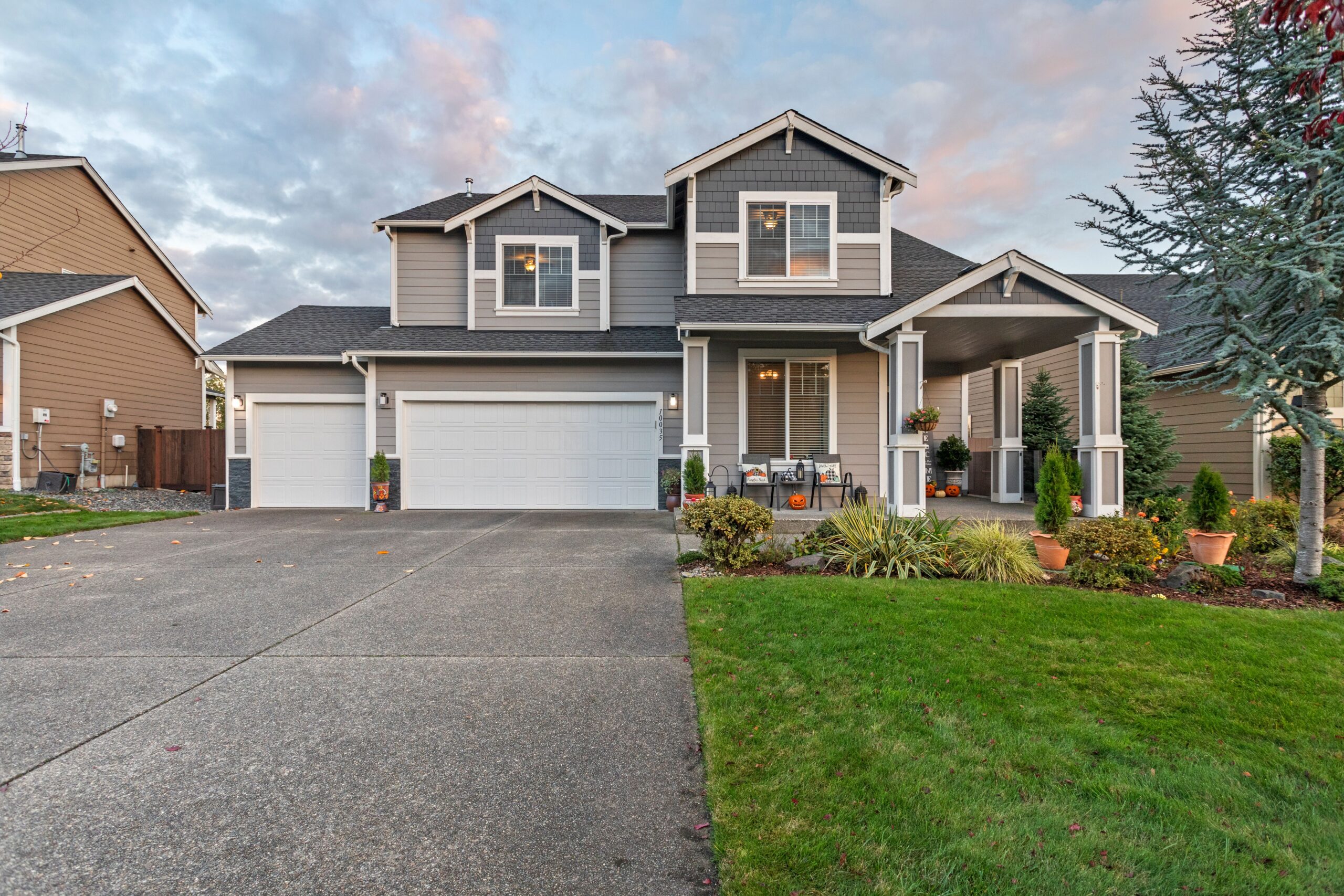 Two-story gray suburban home with a two-car garage, front porch, and a manicured green lawn.
