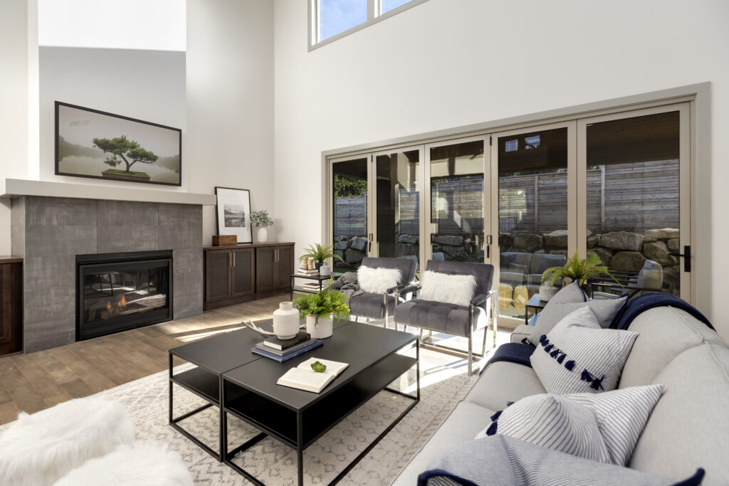 Modern living room with a grey stone fireplace, black coffee table, grey sectional, and large sliding glass doors.