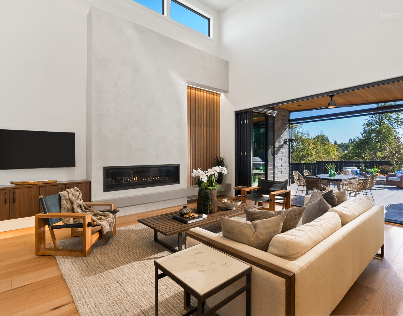 Modern living room with a linear fireplace, light-colored sofa, and large sliding doors opening to an outdoor patio.