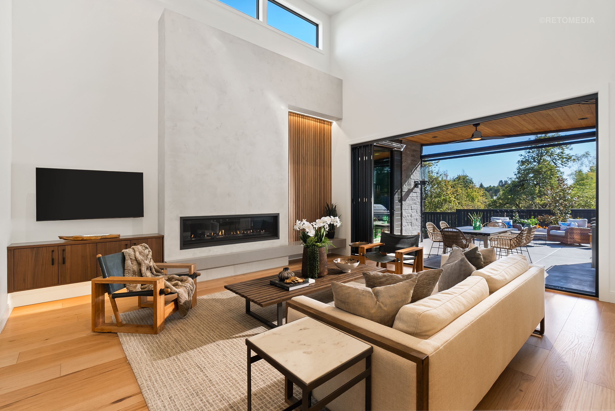 Modern living room with a linear fireplace, light-colored sofa, and large sliding doors opening to an outdoor patio.