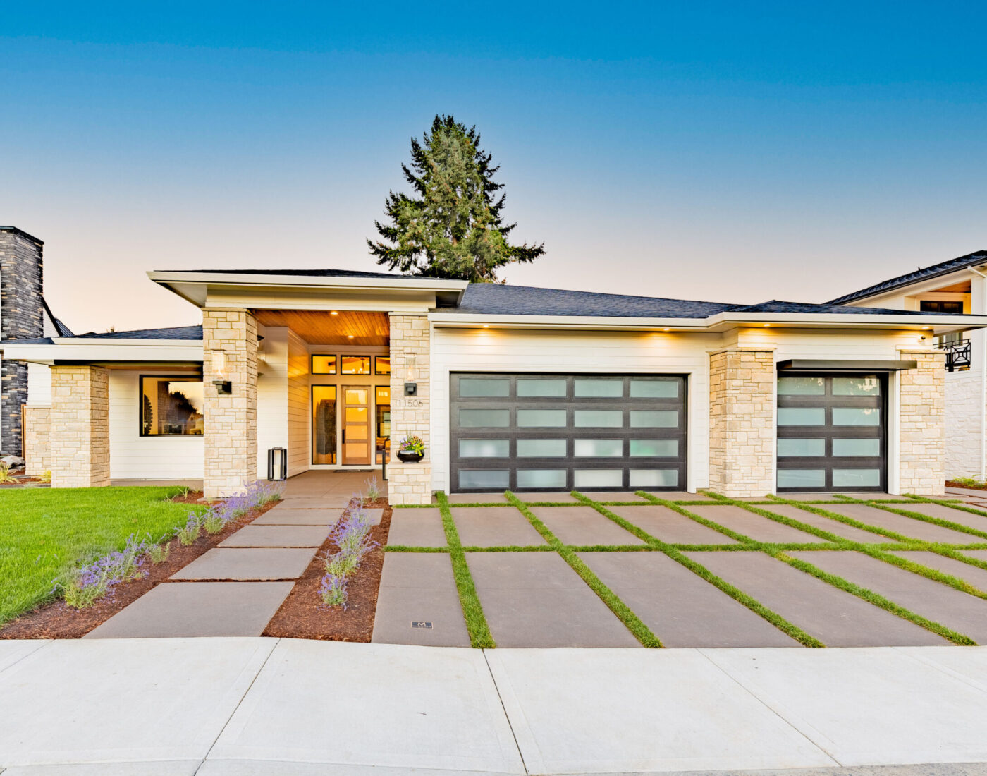 Modern single-story home with white stone accents, frosted glass garage doors, and a geometric concrete driveway.