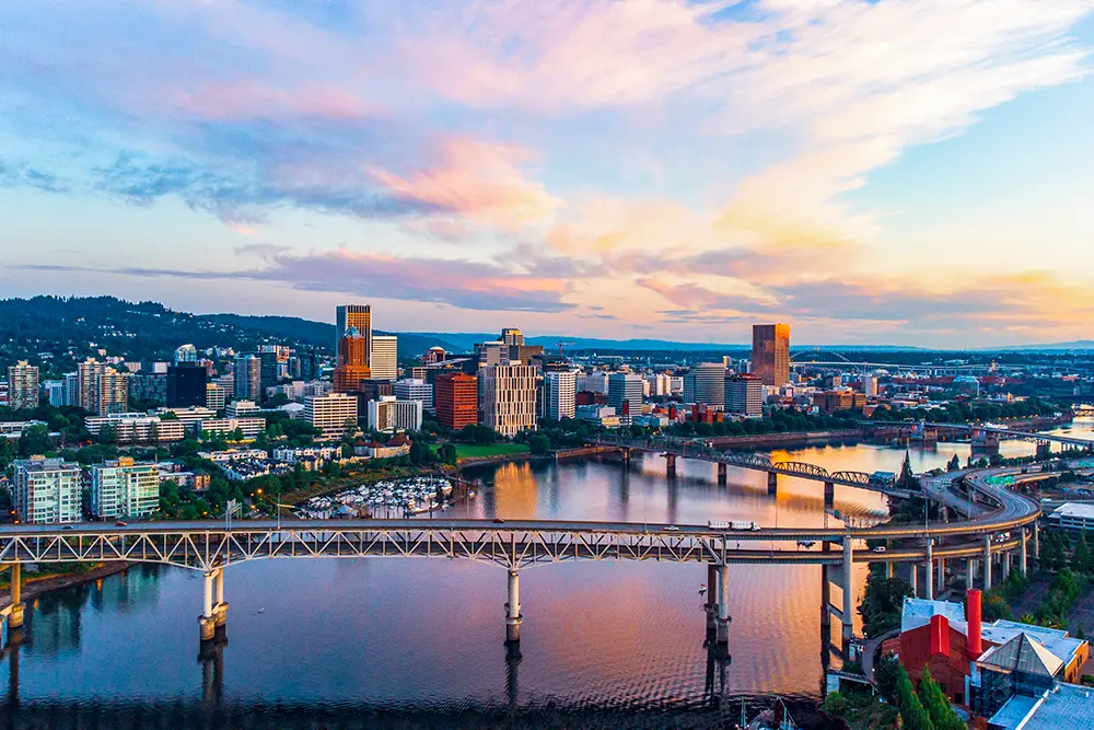 Portland city skyline at sunset with a bridge spanning across the river in the foreground.