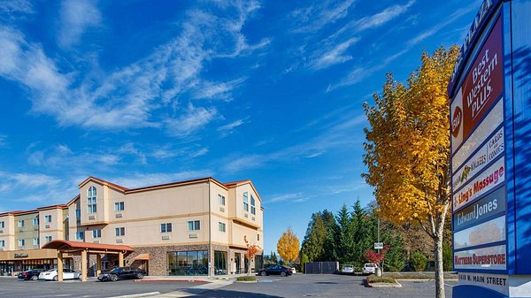 Exterior of a Best Western Plus hotel with a multi-story building, parking lot, and a tall signage pylon.