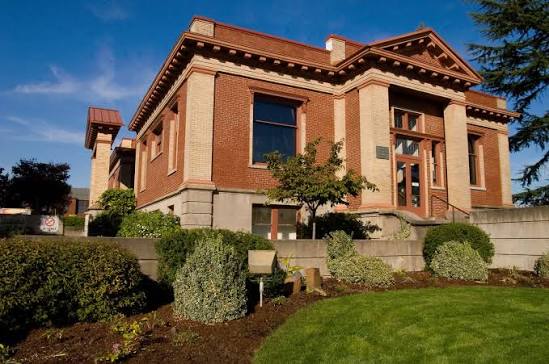 Two-story red brick house with light-colored stone accents, a gabled roof, and manicured shrubbery.