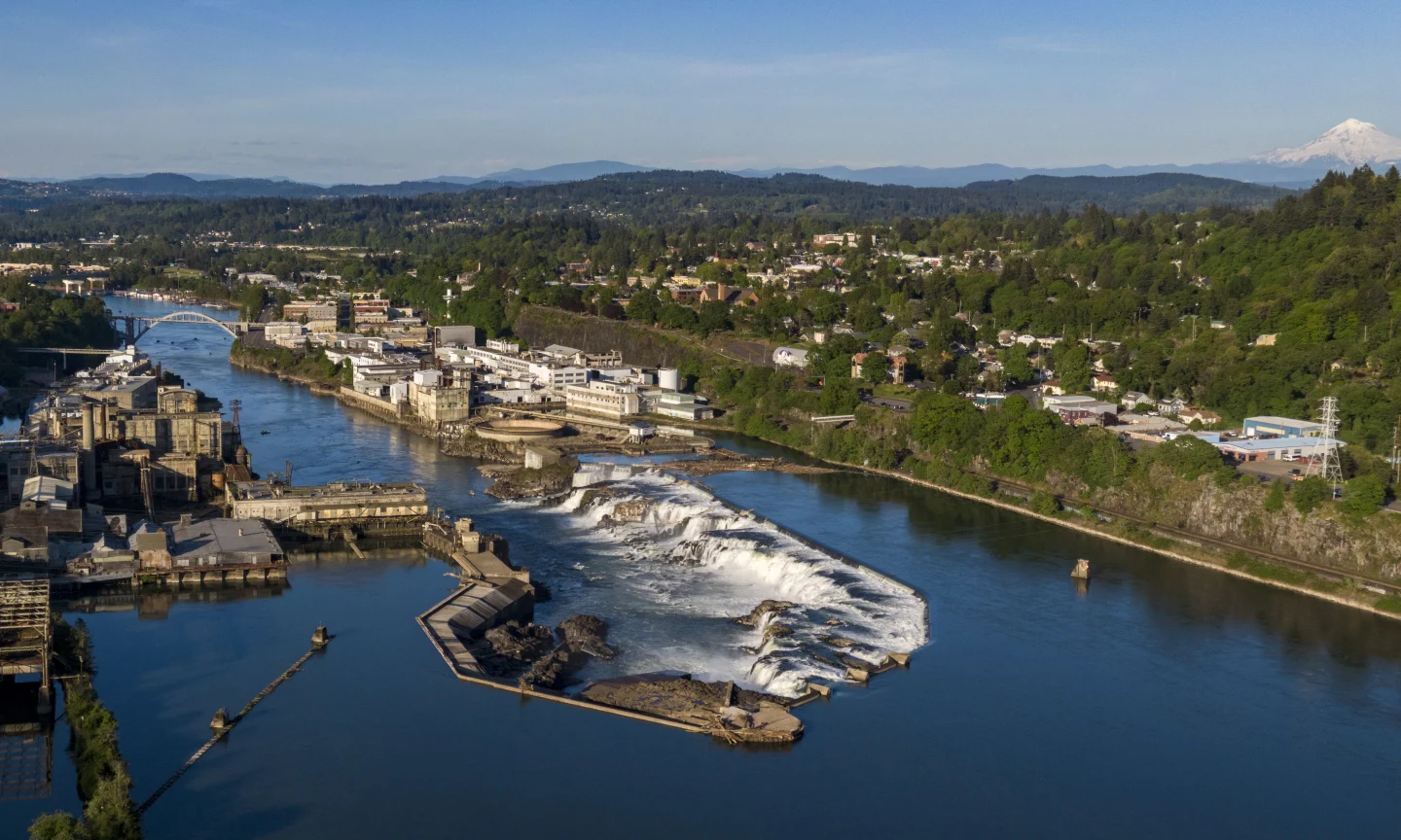 Aerial view of Willamette Falls and surrounding industrial buildings and town under a clear blue sky.