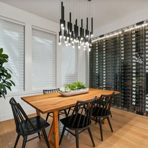 Modern dining room featuring a wooden table with black chairs, a large potted plant, and a floor-to-ceiling wine wall.